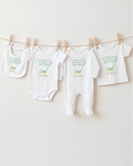 A row of four white baby clothes, including onesies and bibs, hanging on a clothesline.