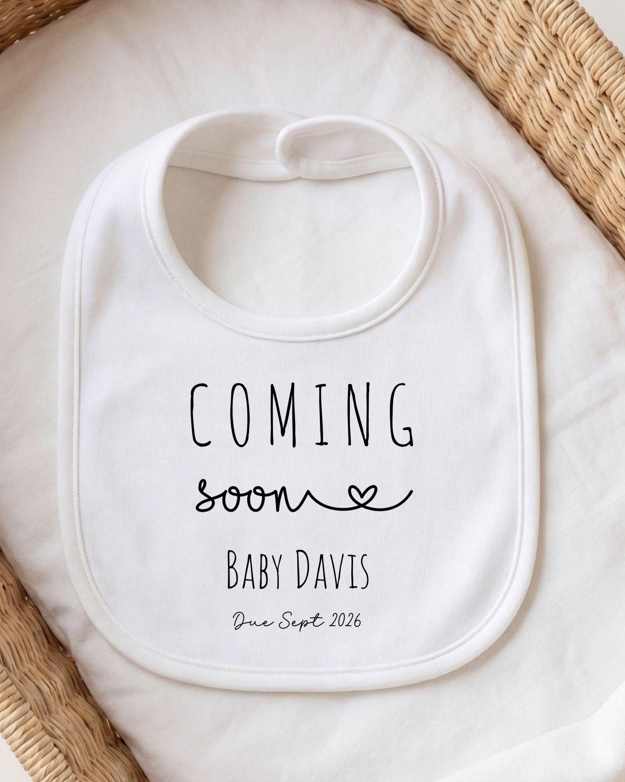 A white bib with the text "COMING soon BABY DAVIS Due Sept. 2026" printed on it.
