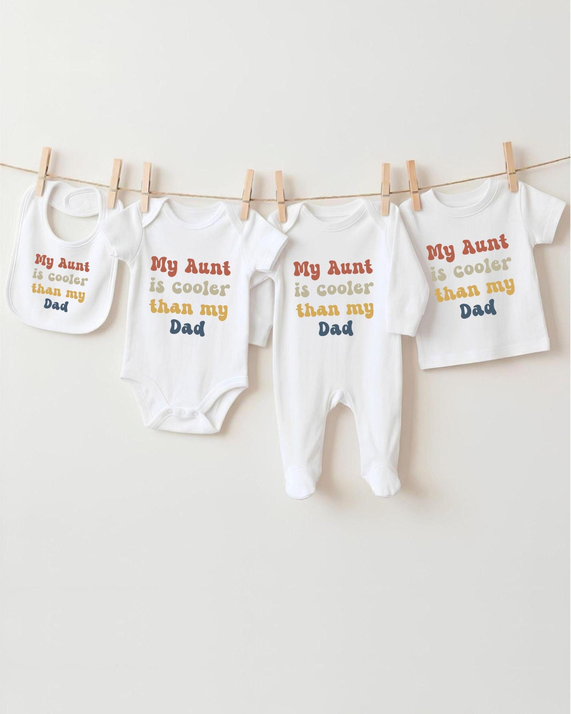a row of four white baby clothes hanging on a clothesline, each with a different message printed on it.