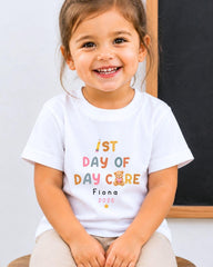 A young girl wearing a white t-shirt with text and a teddy bear graphic, smiling at the camera.