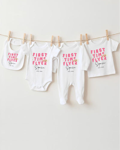 A row of four white baby clothes, including onesies and bibs, hanging on a clothesline.