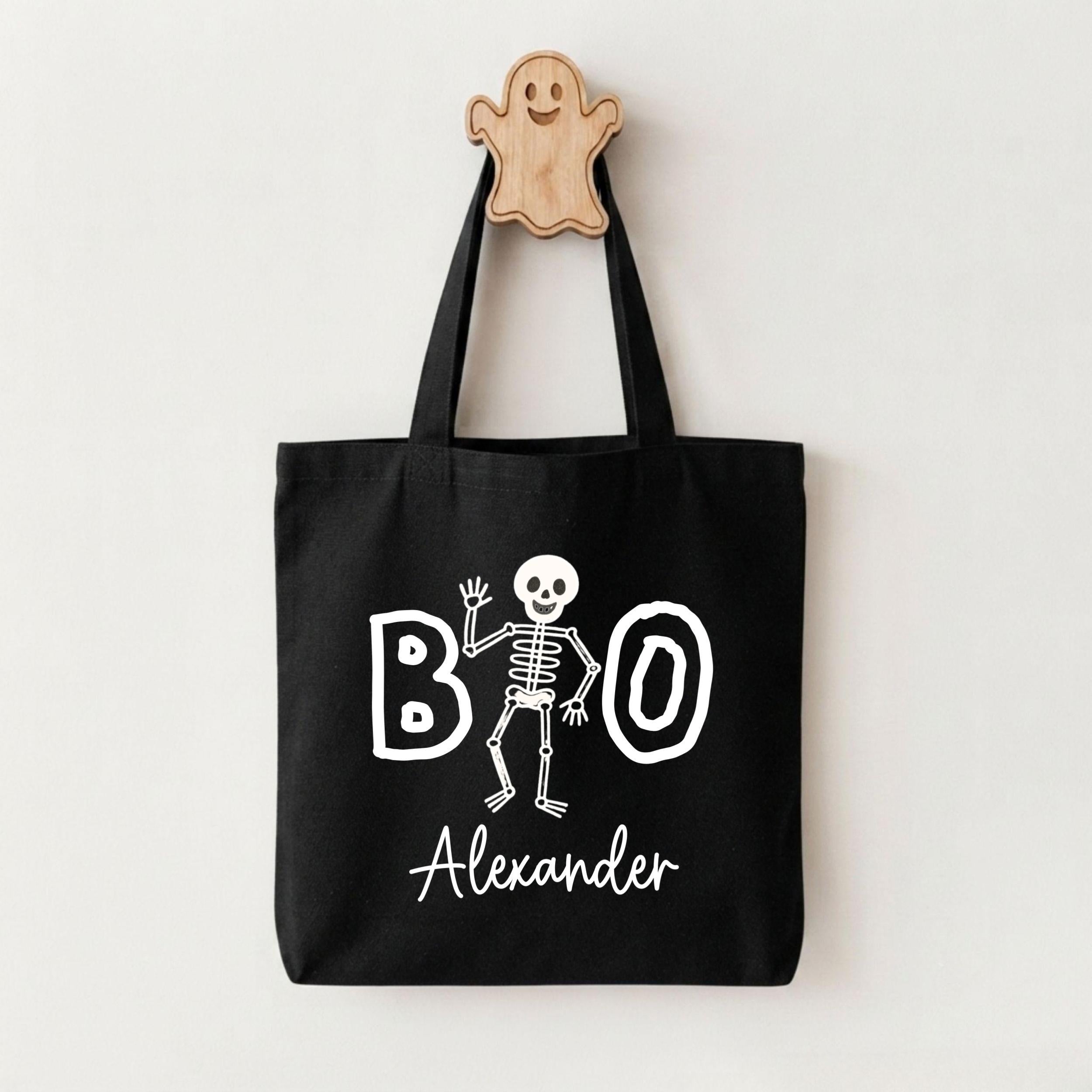 A black tote bag with a skeleton design and the text "BOO Alexander" printed on it.
