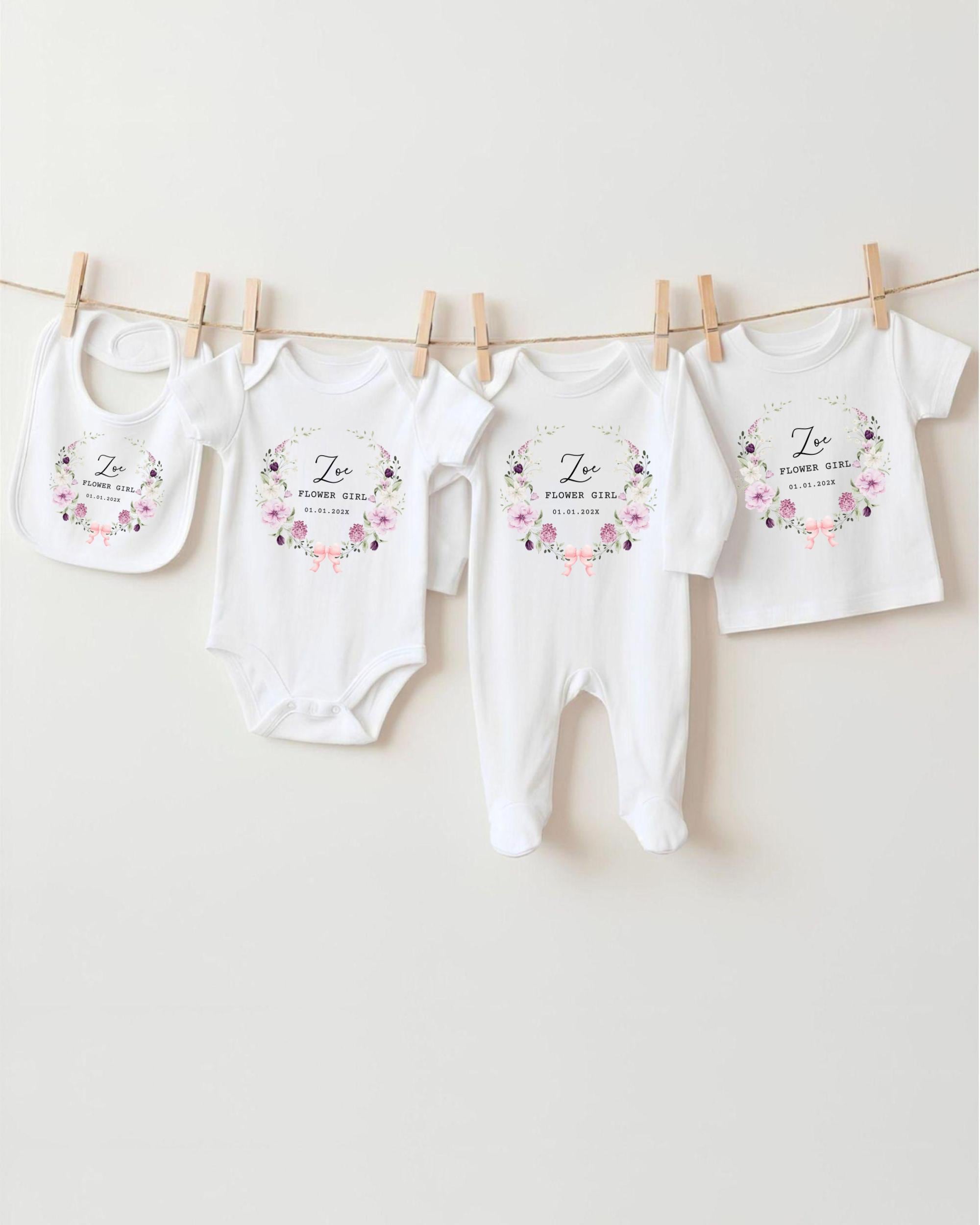 A row of four white baby clothes with floral designs, hanging on a clothesline.