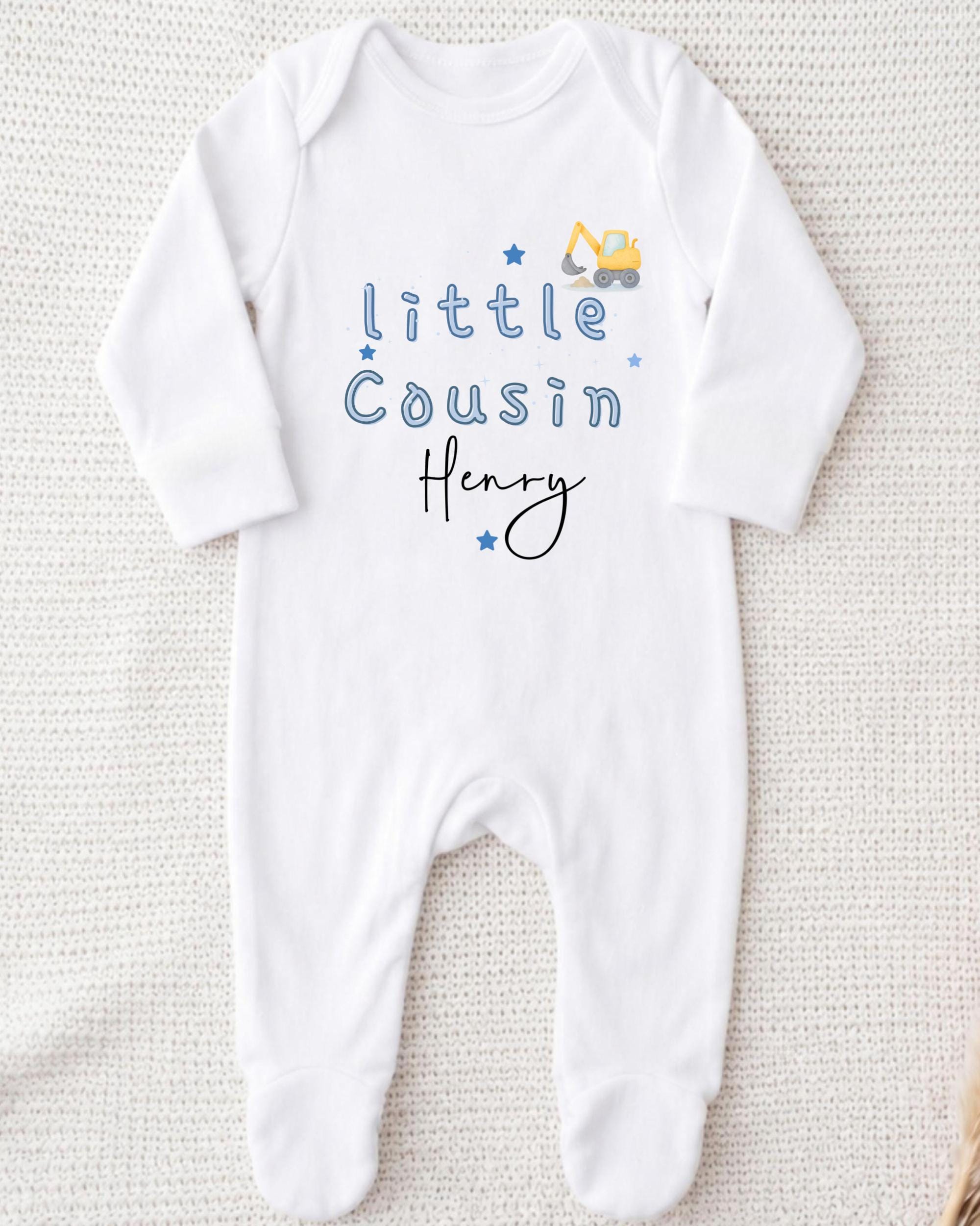 A white onesie with blue text and a small construction vehicle graphic printed on it.