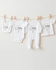 a collection of white baby clothes hanging on a clothesline, each with a personalized name printed on it.