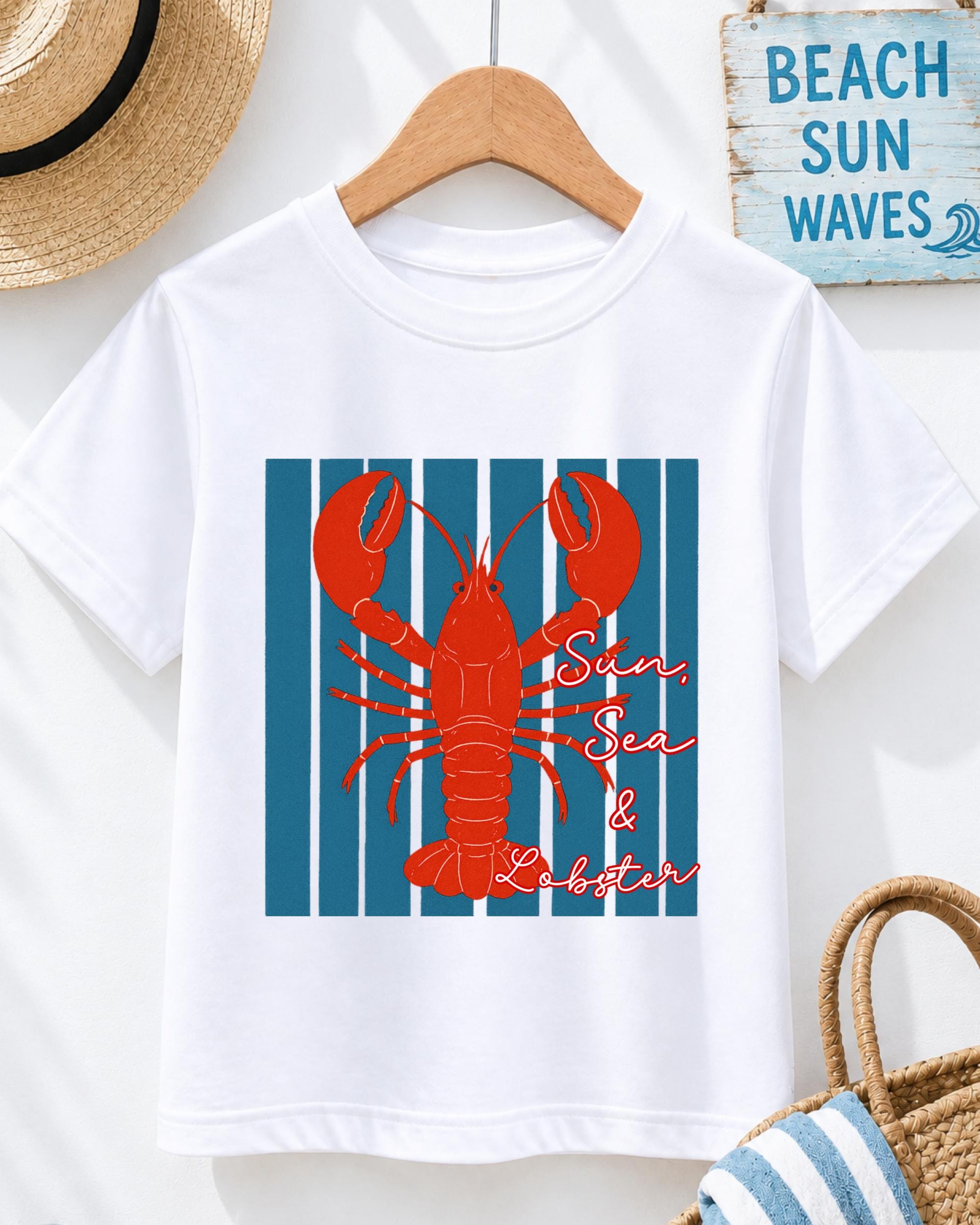 A white t-shirt with a red lobster graphic and the text "Sun, Sea & Lobster" printed on it, hanging on a wooden hanger.