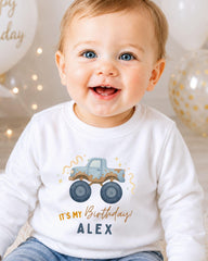 A smiling baby boy wearing a white shirt with a graphic of a truck and the text "It's my birthday! Alex" printed on it.