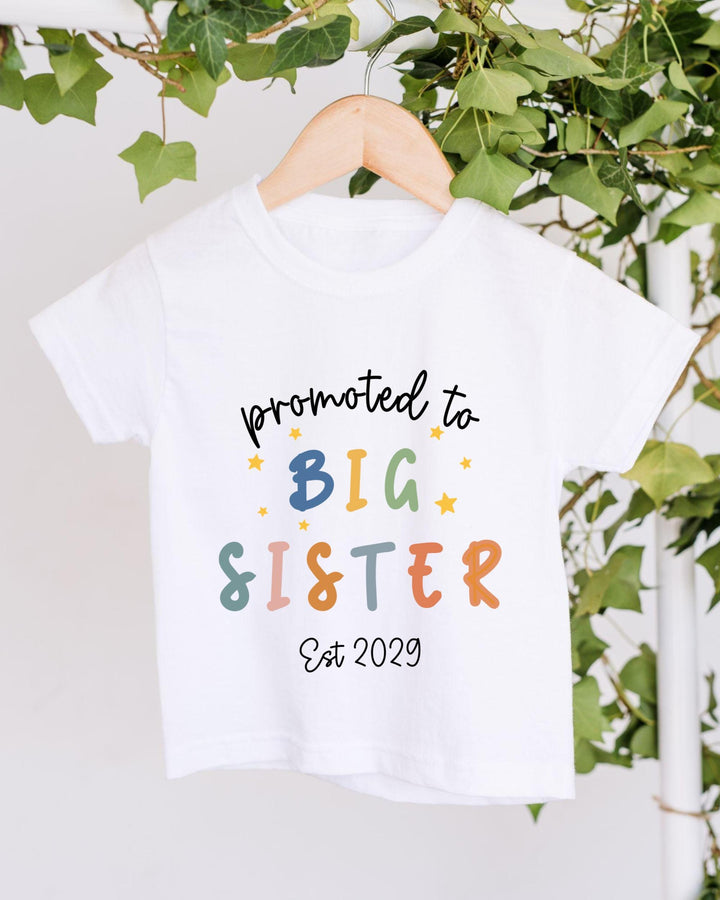 A white t-shirt with text that says "promoted to BIG SISTER Est 2029" printed on it.