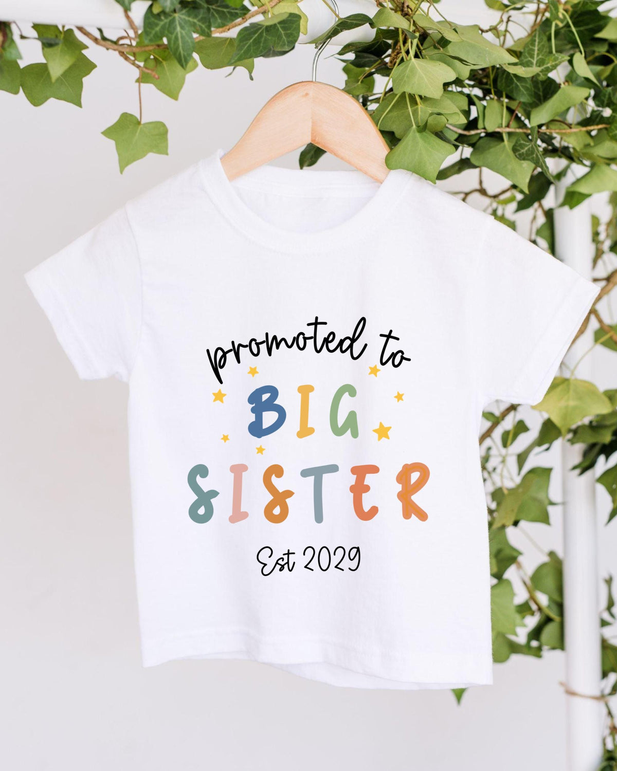 A white t-shirt with text that says "promoted to BIG SISTER Est 2029" printed on it.