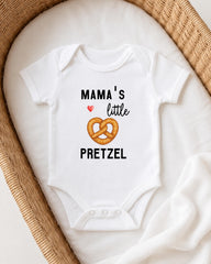 A white baby onesie with the text "MAMA'S LITTLE PRETZEL" printed on it, along with an illustration of a pretzel.