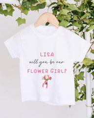A white t-shirt with pink text and a floral illustration hanging on a wooden hanger.