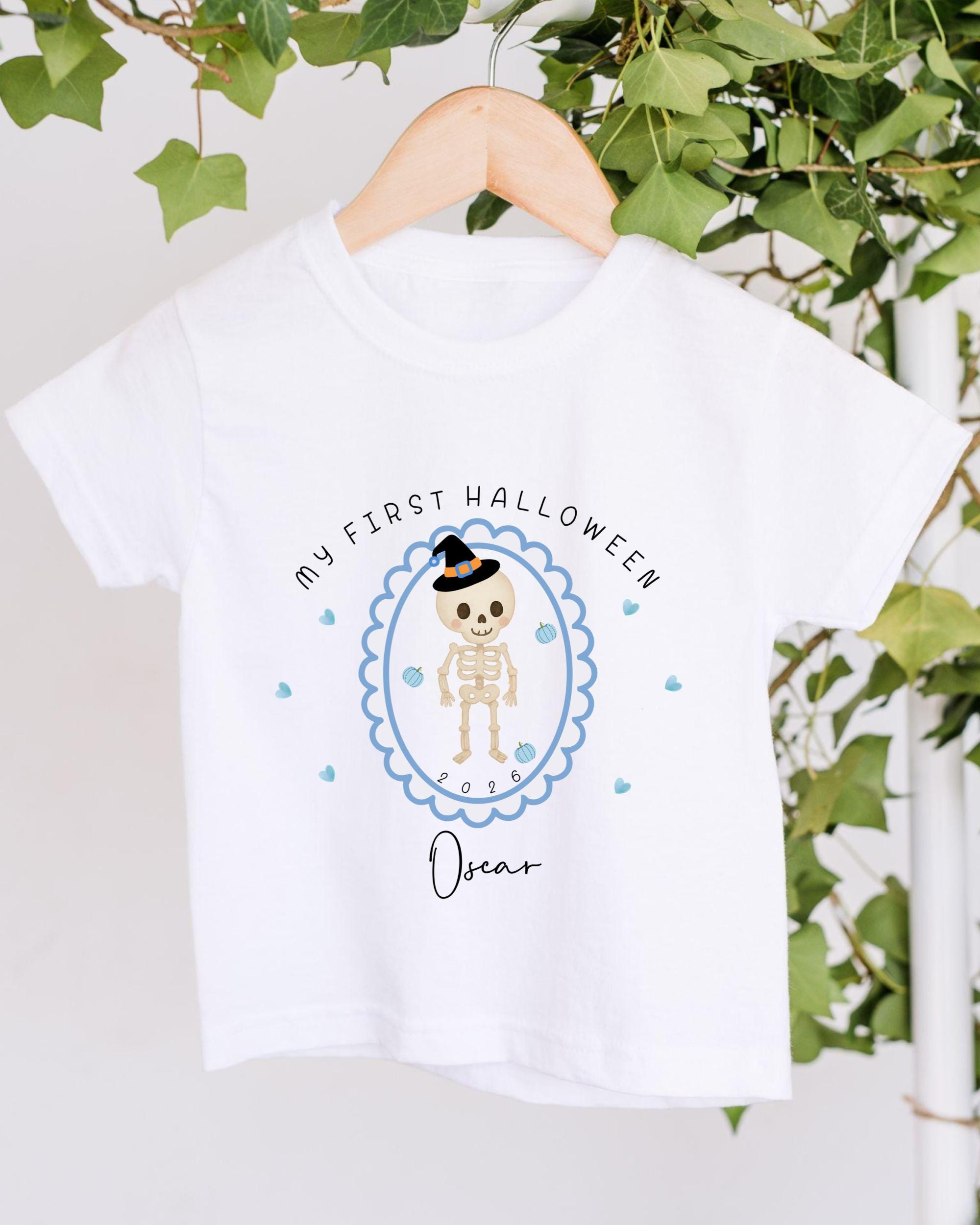 A white t-shirt with a Halloween-themed graphic design, featuring a skeleton wearing a witch's hat and surrounded by blue hearts.