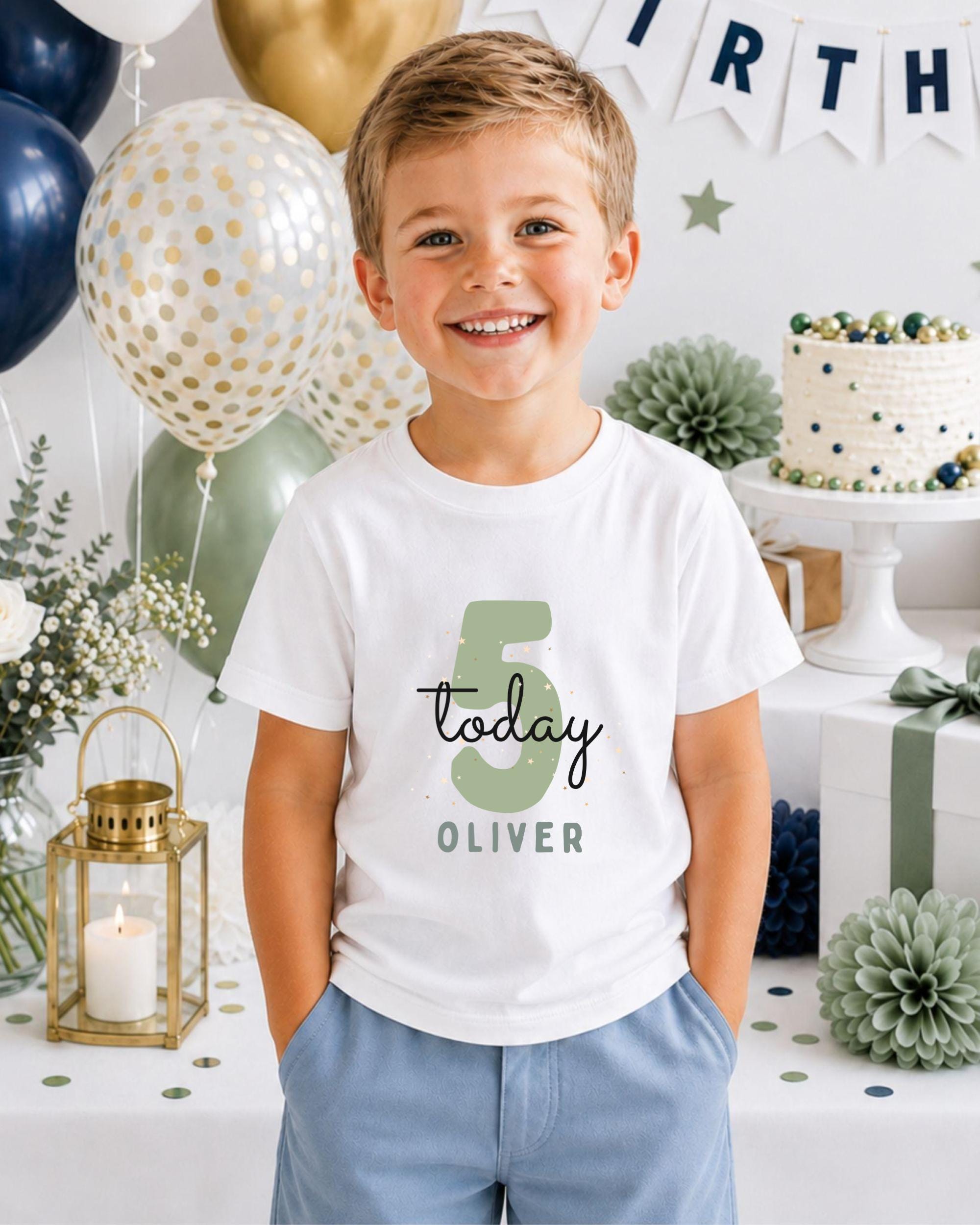 A young boy wearing a white t-shirt with the number 5 and the name "Oliver" printed on it, smiling at the camera. The background includes birthday decorations, balloons, and a cake.