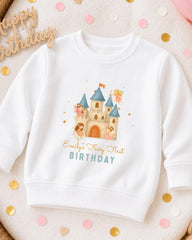 A white sweatshirt with a castle and fairy characters printed on it, along with the text "Emilly's Fairy First Birthday".