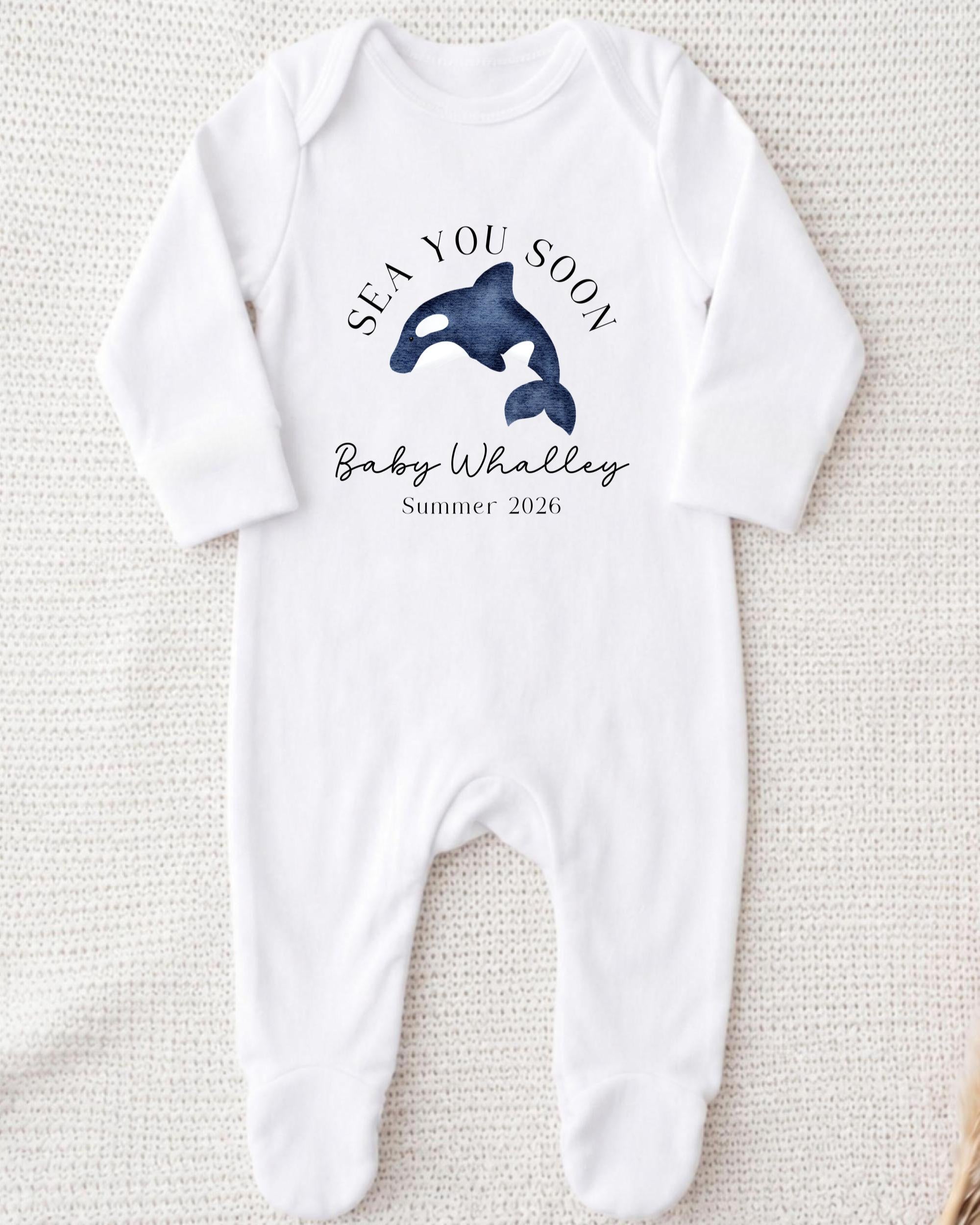 A white onesie with a graphic of a baby whale and text that says "SEA YOU SOON Baby Whalley Summer 2026".