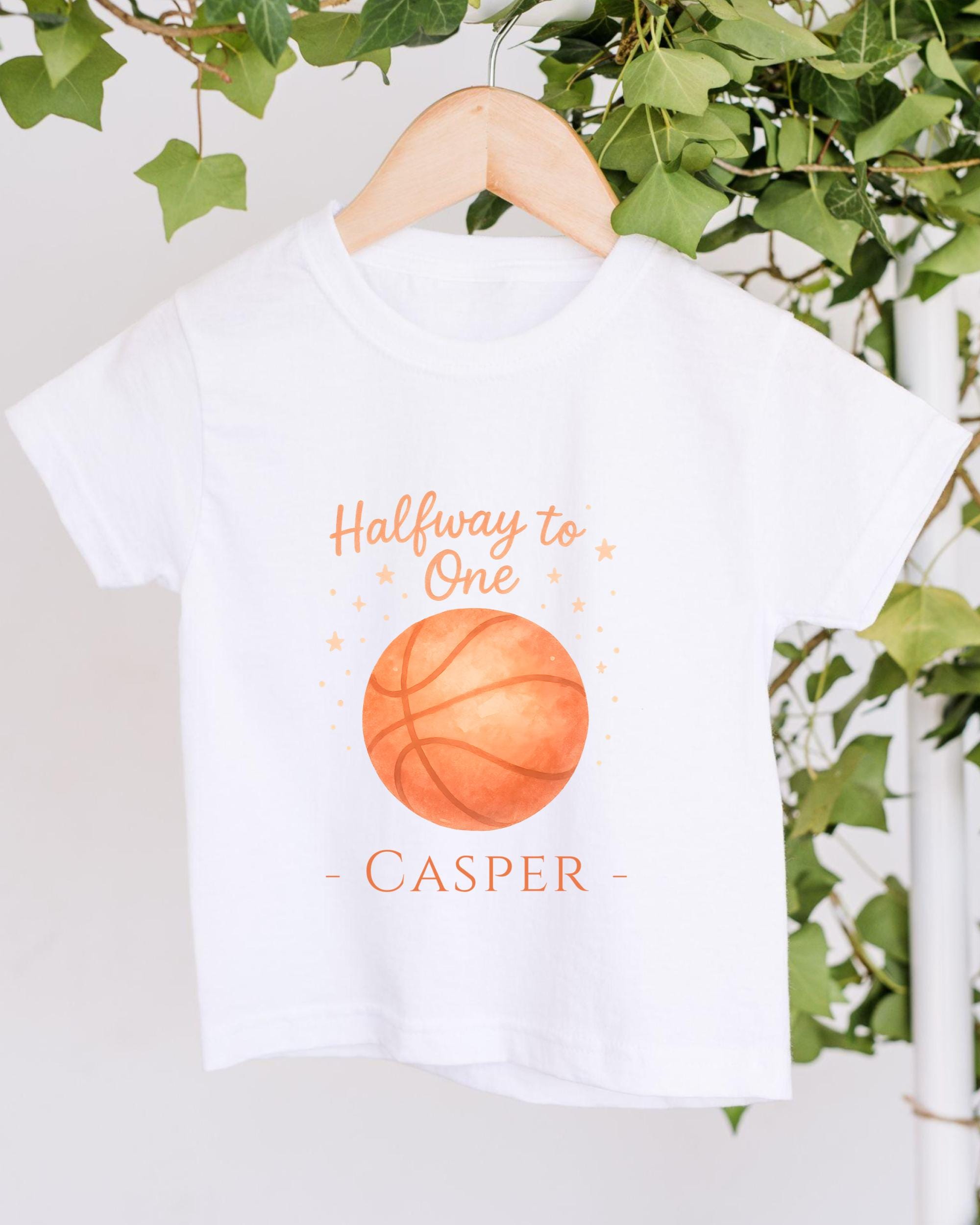 A white t-shirt with a basketball graphic and the text "Halfway to One - CASPER" printed on it, hanging on a wooden hanger.