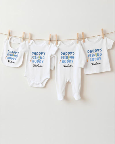A row of white baby clothes with the text "DADMY'S FISHING BUDDY" printed on them, along with the name "Hudson" below.