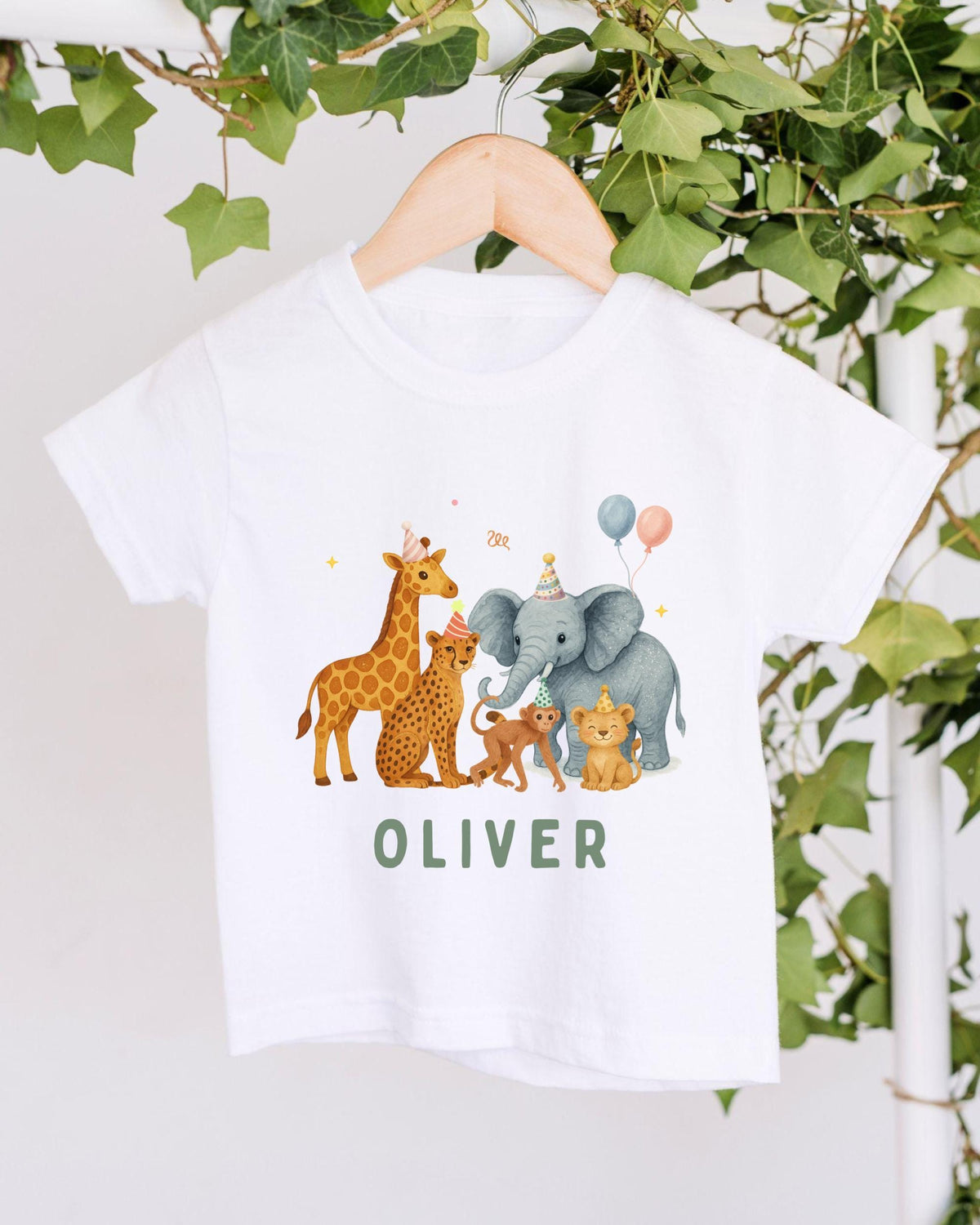 A white t-shirt with a graphic design featuring a giraffe, elephant, and other animals wearing party hats, along with the name "OLIVER" written on the shirt.