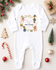 A white onesie with a Christmas-themed design, featuring illustrations of mice and other holiday-themed characters, is displayed on a white background alongside various Christmas decorations.