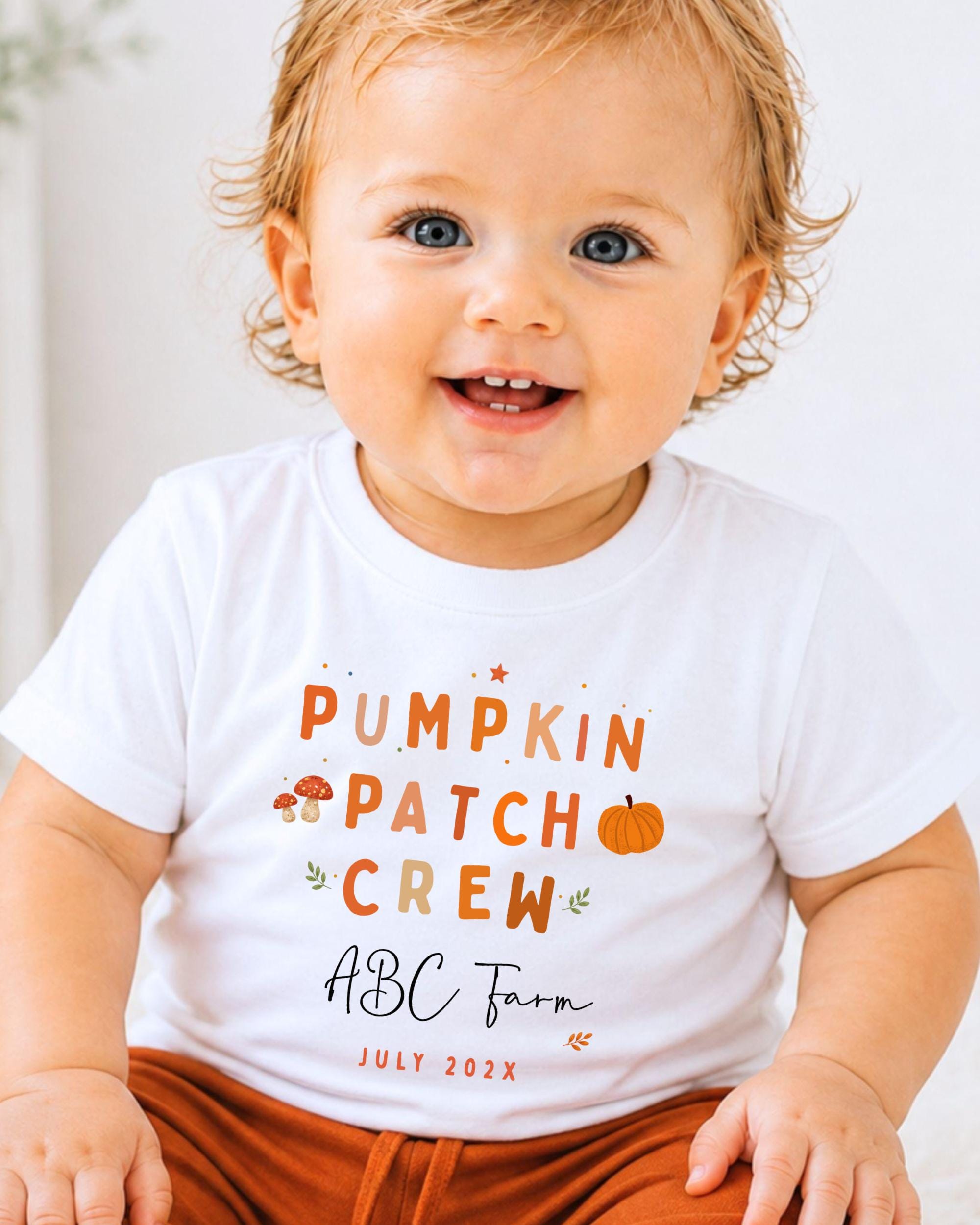 A smiling baby wearing a white t-shirt with text and illustrations related to a pumpkin patch crew.