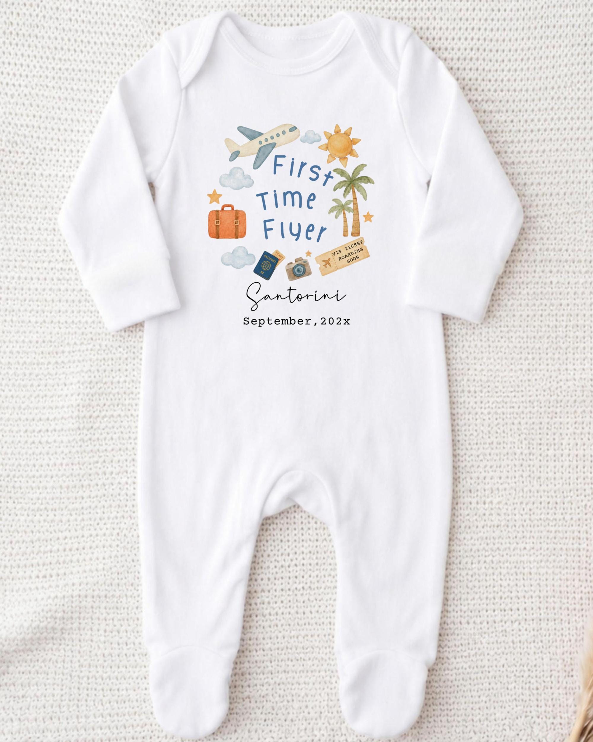 A white onesie with a graphic design on it, featuring a plane, a sun, a palm tree, and various travel-related icons.