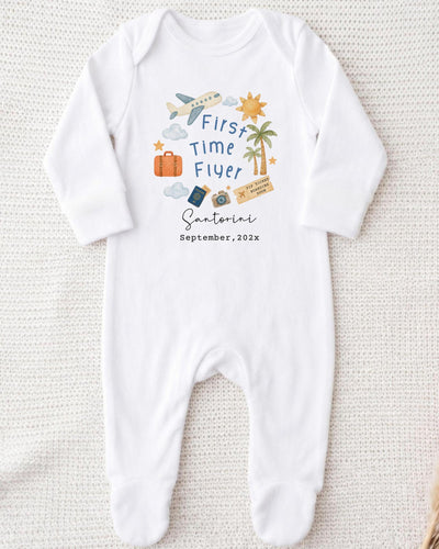 A white onesie with a graphic design on it, featuring a plane, a sun, a palm tree, and various travel-related icons.