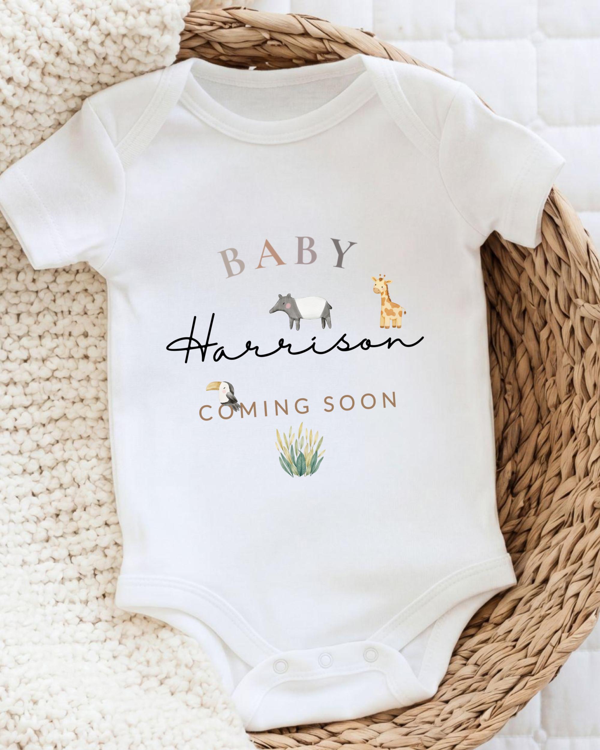 A white baby onesie with the text "BABY Harrison COMING SOON" printed on it, along with illustrations of a giraffe and a bird.