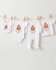 A row of white baby clothes with red and green Christmas-themed designs hanging on a clothesline.