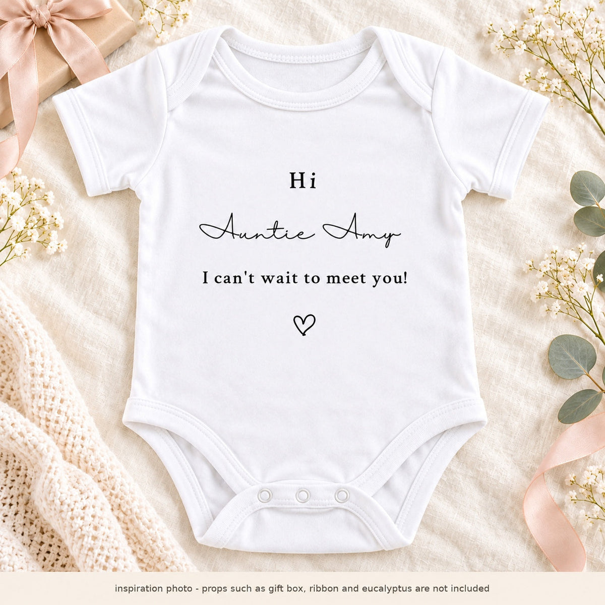 Square pregnancy announcement photo of a personalised Hi Auntie Amy Baby Vest, styled with a beige gift box, pink ribbon and eucalyptus