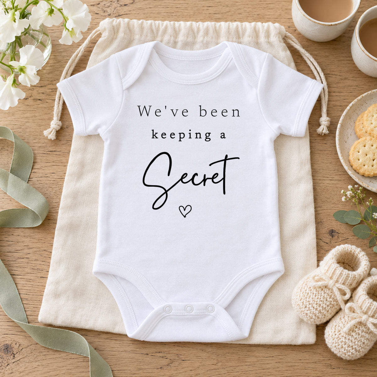 White We've been keeping a Secret Baby Vest on an ivory drawstring gift bag with tea, shortbread, white flowers, cream booties and sage ribbon.