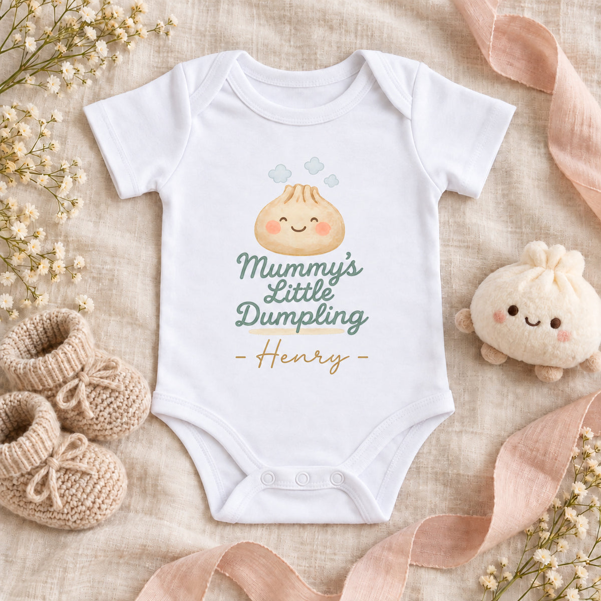 White Mummy's Little Dumpling Baby Vest personalised with Henry, featuring a smiling dumpling and three steam clouds, on ivory linen with beige booties, blush ribbon and a dumpling soft toy.