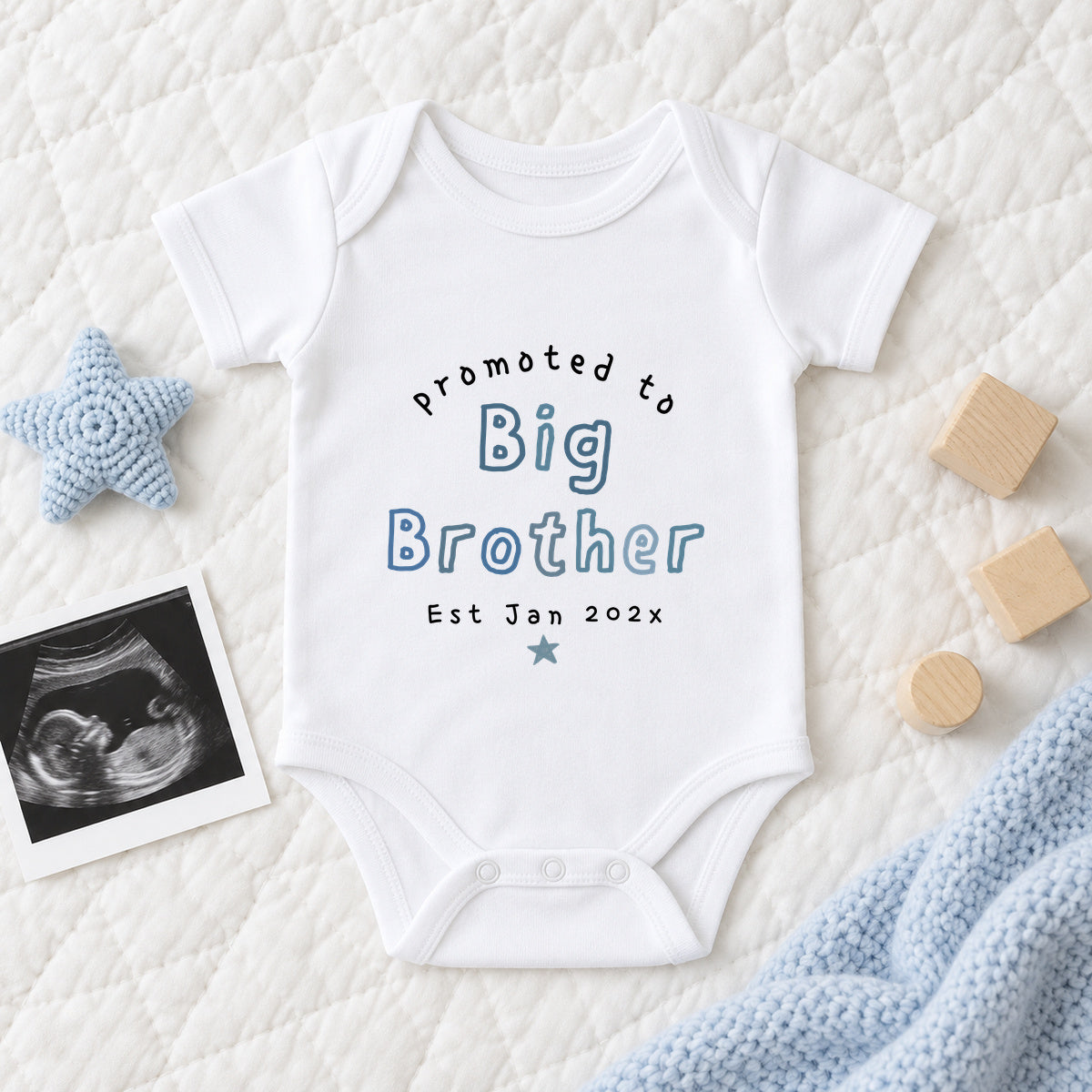 White personalised Promoted To Big Brother Baby Vest with blue outlined lettering and expected date, styled beside a scan photo and soft blue nursery props.