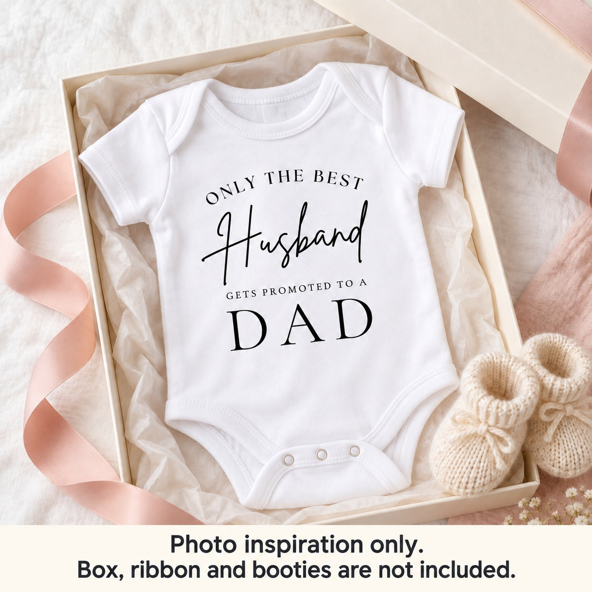 White 'Only the Best Husband Gets Promoted to a Dad' baby vest in an ivory gift box with blush ribbon and knitted booties. Photo inspiration only; box, ribbon and booties are not included.